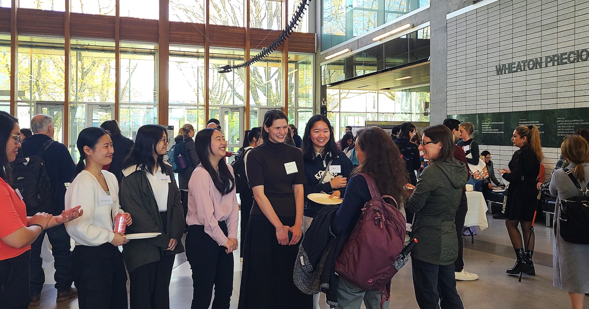 A group of students in the atrium of a building standing around and chatting.