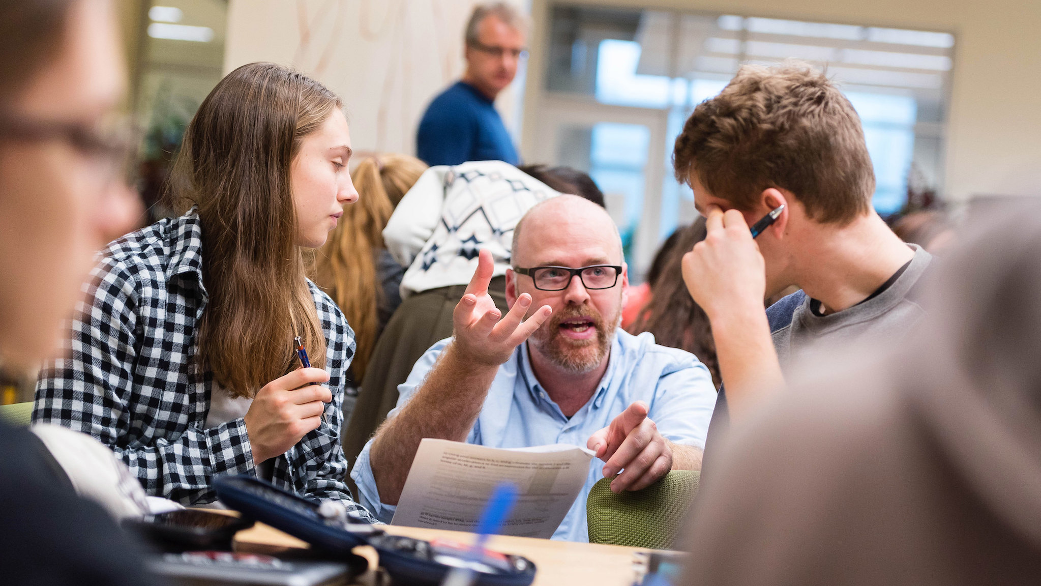 An image of a professor speaking to two student sitting at a table.