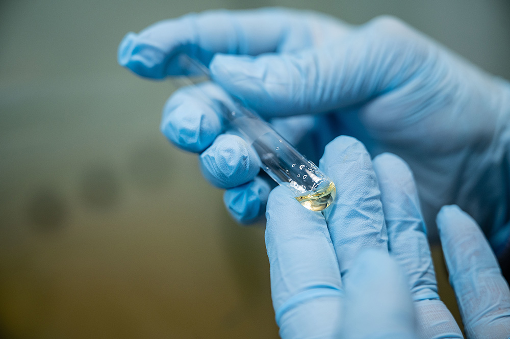 Two hands in blue gloves holding a tube containing liquid