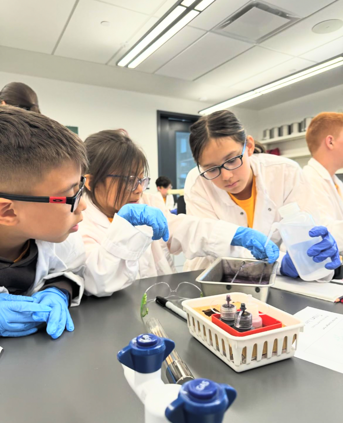 A group of Indigenous youth wearing lab coats with lab equipment.