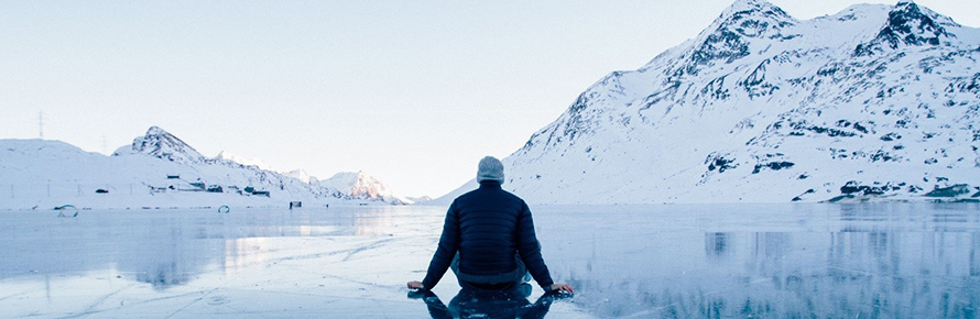 A person sitting in front of a lake and snowy mountain range.