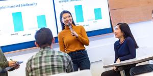 A person stands in front of a room presenting a powerpoint.