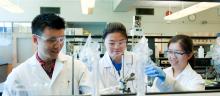 Three students in lab coats and goggles are working on a chemistry experiment.