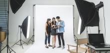 Three people stand together in a photo studio looking at a camera.